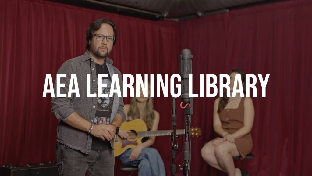 John Escobar stands in front of two performers and AEA microphones. The words AEA Learning Library are across the image.